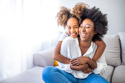 Shot of an adorable little girl and her mother in a warm embrace at home. Loving young mother laughing embracing smiling cute funny kid girl. Head shot close up happy young mother bonding little adorable daughter