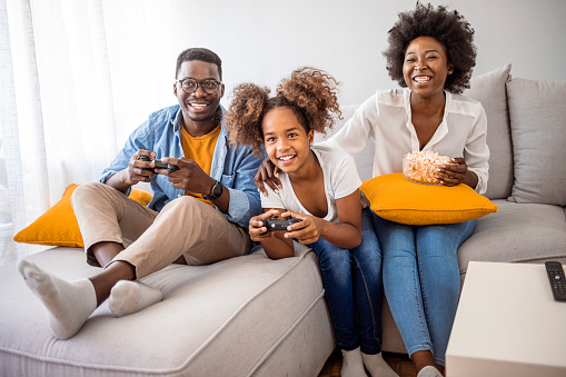 Smiling family sitting on the couch together playing video games. Playful family playing video games together in a living room. Happy family sitting on a sofa and playing video games.