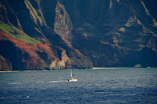 Ocean-level view of a sailboat cruising past the magnificent Napali Coast on Kauai