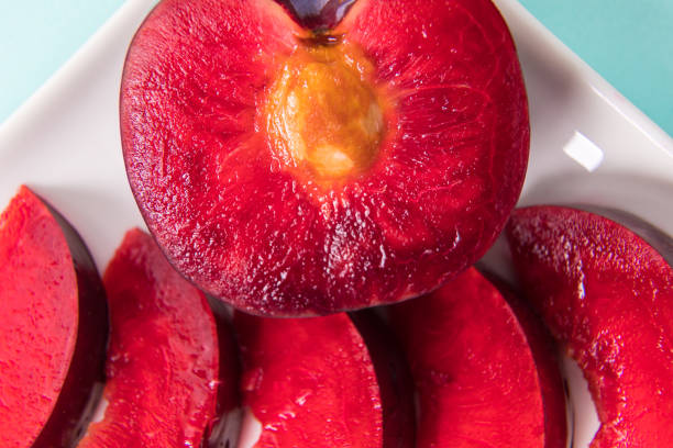 istock On a white saucer, a large plum, cut in half, with slices next to it. 1326980593