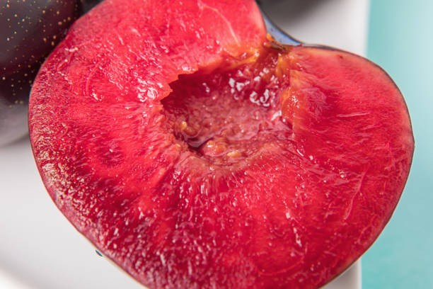 On a white saucer is a large plum, cut in half, and next to it is a whole plum. The pulp of red berries. Close-up.