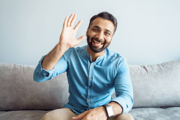 Headshot portrait of handsome indian man with friendly smile waving to camera Headshot portrait of handsome young indian business man with friendly confident smile feeling happy and positive waving to camera saying hello with raised hand gesture making video call. Webcam view webcam view man stock pictures, royalty-free photos & images