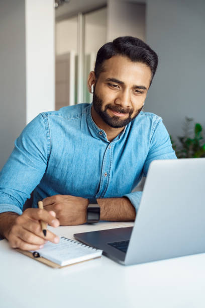 Indian man using laptop and earphone for online studying and e-learning stock photo