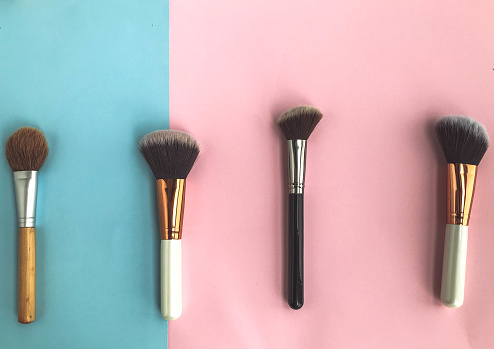 brushes on a pink-blue background. applying makeup, beauty with a natural base. using brushes to distribute powder, foundation, blush and highlighter.
