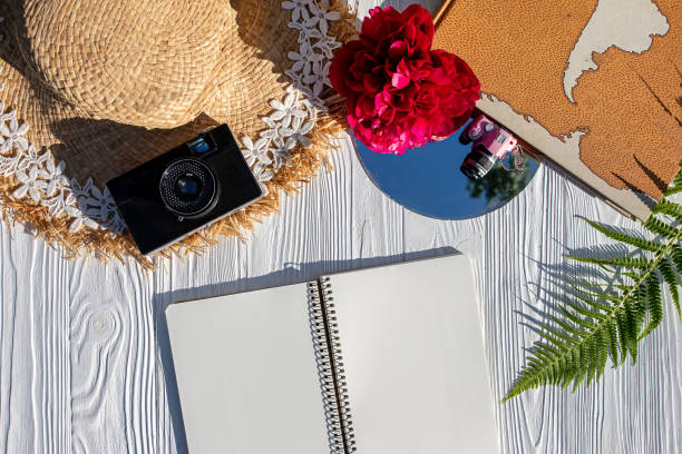 istock Summer vacation concept flat lay. Straw hat, film camera, world map on white table with a clean notebook. Copy space 1326995898