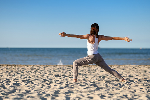 Young woman doing yoga in warrior pose in the beach.
