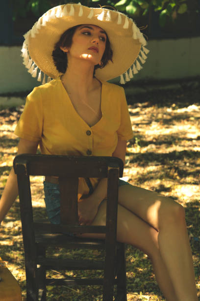 wiejska kobieta siedzi na drewnianym krześle ze słomkową koszulą i jeansowymi spodenkami. - fashion women denim farm zdjęcia i obrazy z banku zdjęć