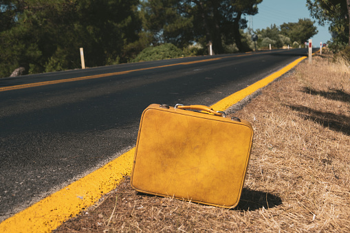 Close up shot of a vintage yellow colored suitcase near the country roadside.