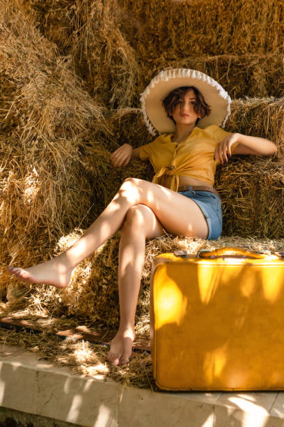 portrait of a woman with a straw hat sitting in a hayloft. - fashion women denim farm imagens e fotografias de stock