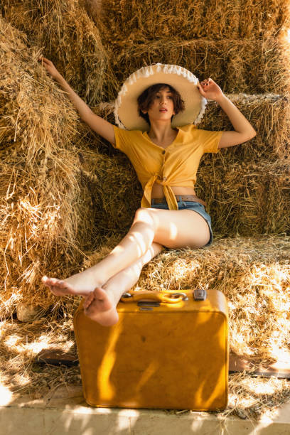 portrait of a woman with a straw hat sitting in a hayloft. - fashion women denim farm imagens e fotografias de stock