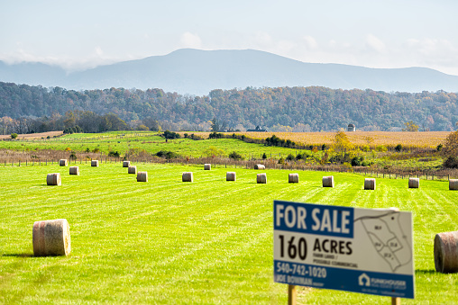 Elkton, USA - October 27, 2020: Hay roll bales on countryside field in Shenandoah Valley Virginia mountains with sign for acres for sale