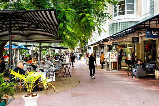 Miami Beach, USA - January 17, 2021: Famous Lincoln road shopping street with people eating on sidewalk patio restaurant cafe outdoor dining chairs on sunny winter day