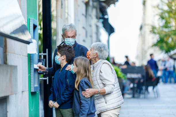 starsza para z wnukiem i wnuczką z maskami na twarz używa bankomatu. - pin up girl zdjęcia i obrazy z banku zdjęć