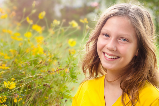 A girl of elementary age walks through a field of flowers in the summertime and smiles.