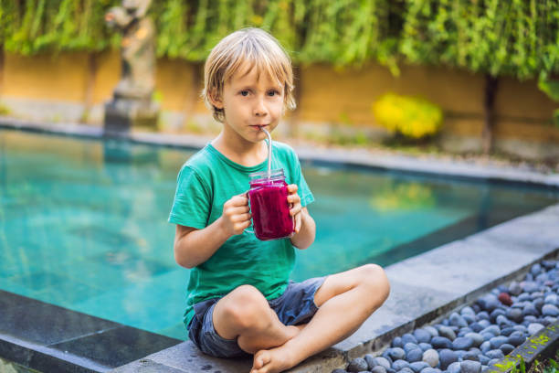 istock Boy drinks dragon fruit smoothie with steel drinking straw by the pool 1327017678