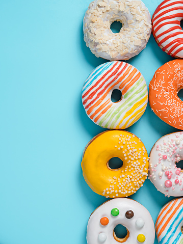 Delicious glazed donuts on blue background. Vertical flat lay - set of different colorful donuts or doughnuts on blue with copy space for text or design. Bright sun light with hard shadows.