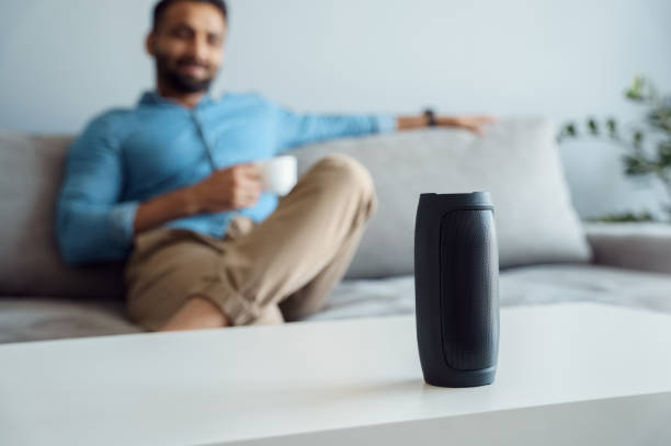 istock Young man on sofa listening small portable wireless speaker at smart home 1327027918