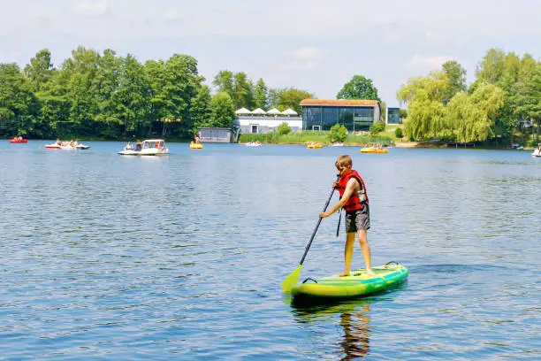 Kid boy paddling on sup board on a lake. Active child on modern trendy stand up paddle board. Summer outdoors vacations activity for family and children. Watersport activieties
