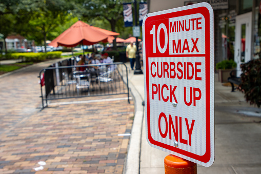 A street sign marks a parking space for curbside pick up only in a downtown district near businesses and a sidewalk cafe.