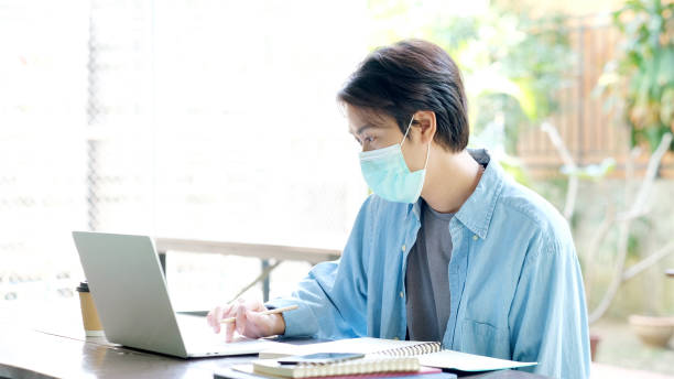 istock Young asian campus student man wearing protection mask working with laptop computer while online study in campus, coronavirus prevention in university, social distancing, online learning 1327034606