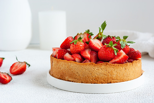 Whole summer vegan strawberry pie on white table, close-up