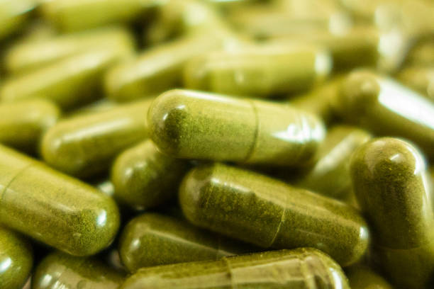 Green chlorella pills or green barley pills in bowl isolated on white background.