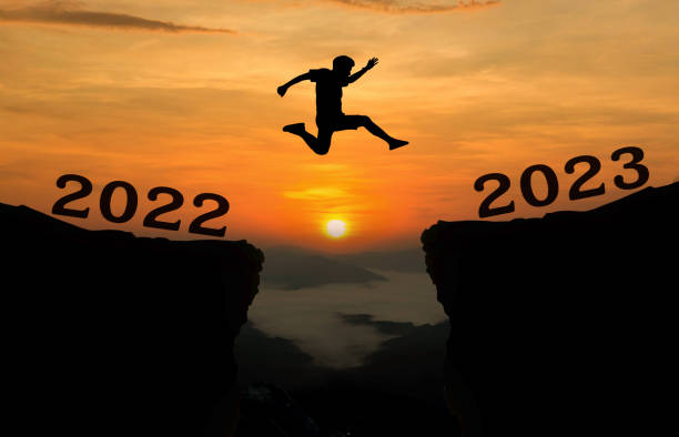 un joven salta entre los años 2022 y 2023 sobre el sol y a través de la brecha de la silueta de la colina por la noche colorido cielo. feliz año nuevo 2022. - intend fotografías e imágenes de stock
