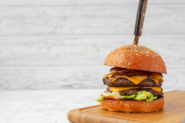 hamburguesa con queso doble servida sobre tabla de madera sobre fondo borroso blanco - hamburger burger symmetry cheeseburger fotografías e imágenes de stock