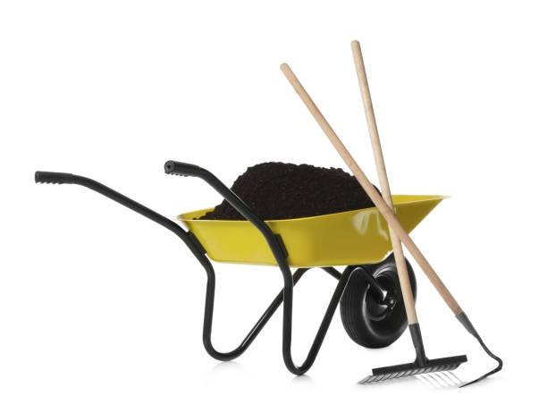 istock Wheelbarrow with soil, rake and hoe on white background. Gardening tools 1327053983