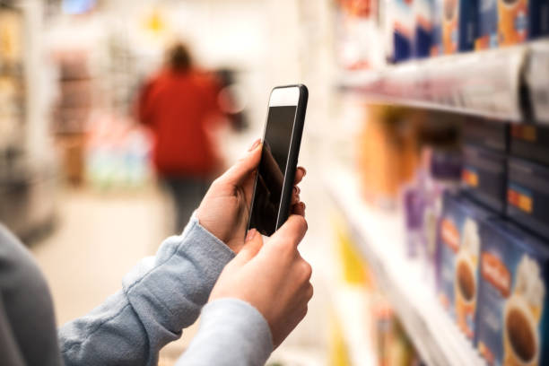 istock Woman's hand holding smart phone on supermarket blur background. 1327055849