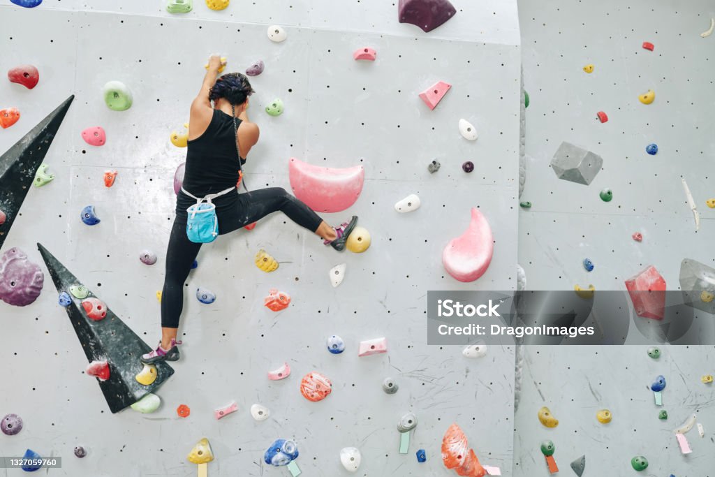 Fit Athlete Climbing up Bouldering Wall Fit athlete climbing up bouldering wall without auto belay devices, view from the back Indoors Stock Photo
