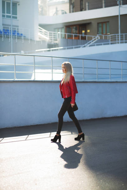 istock Stunning blonde model wearing red jacket walking down the street with sun light 1327061105