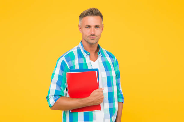 istock man with folder yellow background. Businessman hold book for notes. guy has notepad for writing. handsome school or university teacher. adult man student holding notebooks. Inspired to work hard 1327062540