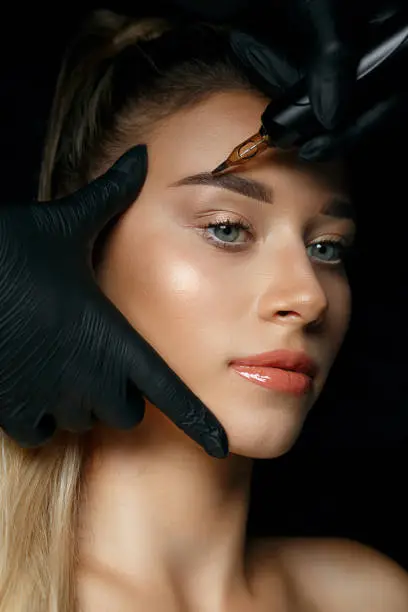 Beautician hand applying eyebrow permanent makeup on a pretty woman face