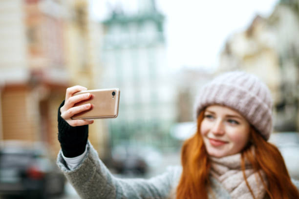 istock Beautiful ginger woman in winter apparel taking selfie on her mobile phone. Empty space 1327070533