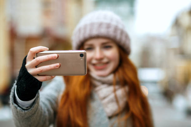 istock Joyful red head model in winter apparel taking selfie on her mobile phone. Empty space 1327070540