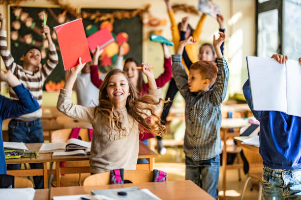 istock Playful elementary students celebrating the end of a school year in the classroom. 1327071433
