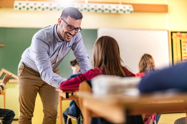 istock Happy male teacher assisting his students on a class at elementary school. 1327072366