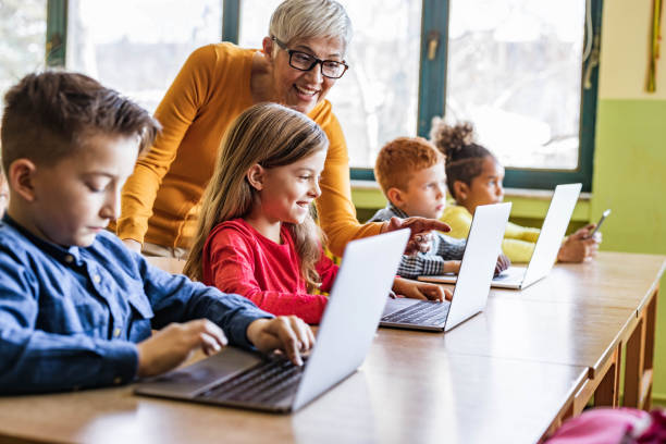 szczęśliwa dojrzała nauczycielka pomagająca swoim uczniom w zajęciach komputerowych w szkole. - elementary school education elementary student teacher zdjęcia i obrazy z banku zdjęć