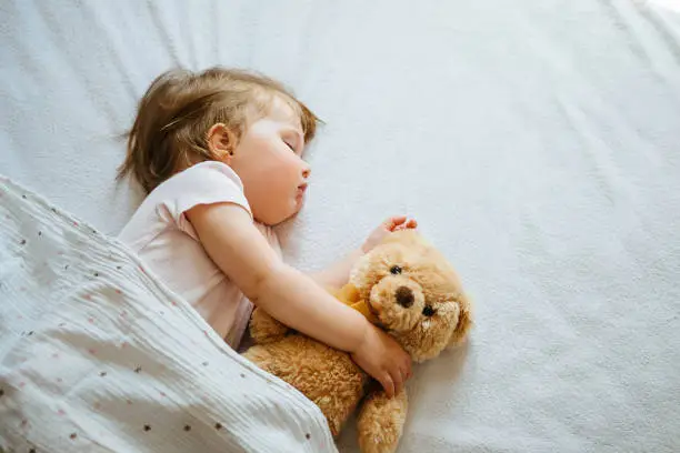 Photo of Little baby sleeping on bed embracing soft toy, free space