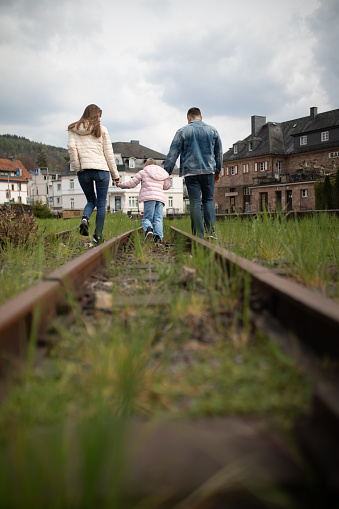 Family with child walking along the railroad, view from behind.