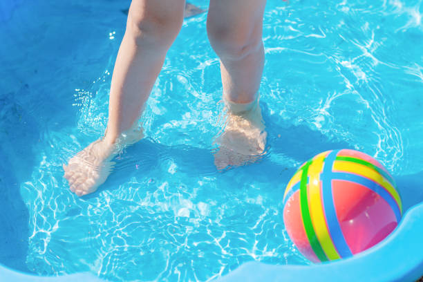 A small child's feet are in the water in a blue shallow pool, a colored ball floating nearby. A small child's feet are in the water in a blue shallow pool, a colored ball floating nearby shallow stock pictures, royalty-free photos & images