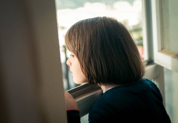 istock Portrait Of Boy Looking Through Window At Home 1327084682