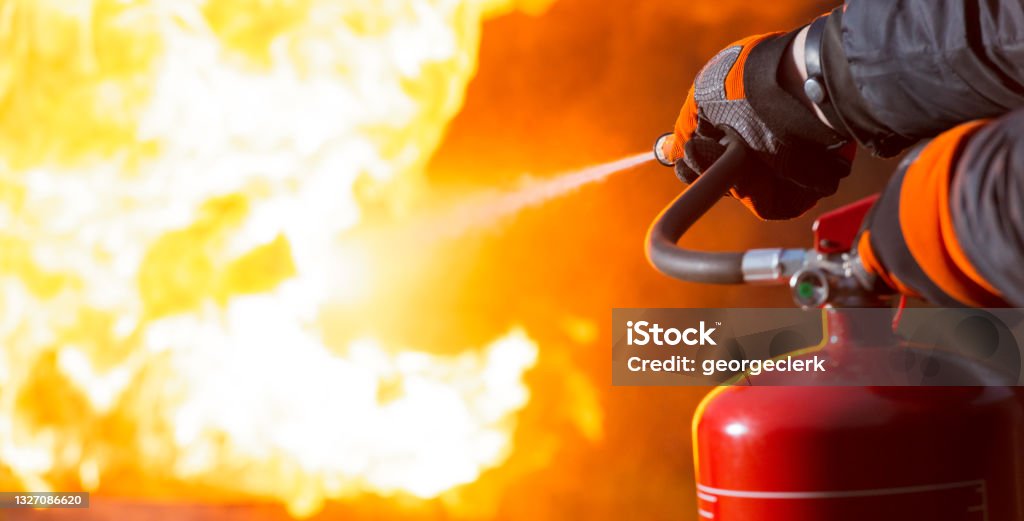 Using a fire extinguisher Close-up showing a person pointing the nozzle of a fire extinguisher at the base of a large fire. Fire Extinguisher Stock Photo