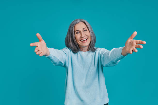 Mature beautiful woman looking at camera and keeping arms outstretched Mature beautiful woman looking at camera and keeping arms outstretched while standing against blue background arms outstretched stock pictures, royalty-free photos & images