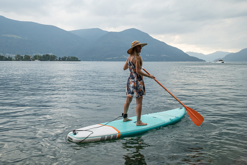 She stands on a paddle board enjoying the lake in Summer, storm approaching. Ticino canton, Switzerland