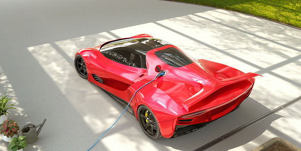 A high rear view of a generic red electric sports car with a blue electric charger attached parked on a light concrete driveway with cast shadows from an overhead pergola. On the edges we see a grass lawn, plants and a watering can. With copy space.