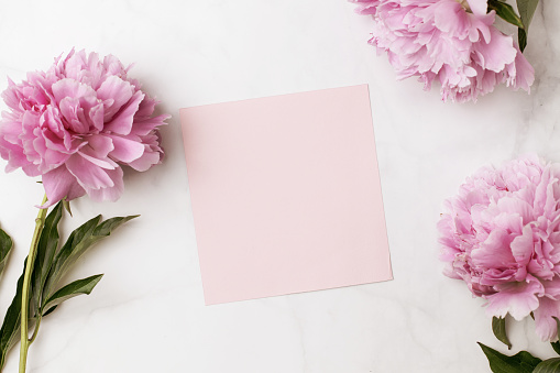 Florist at work: pretty woman making summer bouquet of peonies on a working gray table. Kraft paper, scissors, envelope for congratulations on the table. View from above. Flat lay composition.