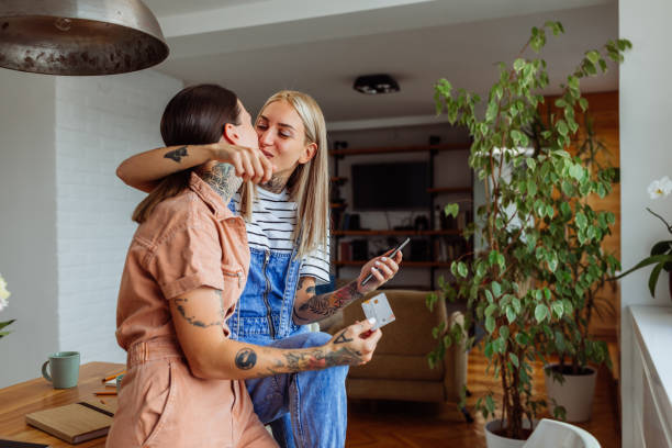 A couple stands in a stylish living room with natural light, holding a microphone and an acoustic guitar, with a vintage bike and various musical instruments in the background.