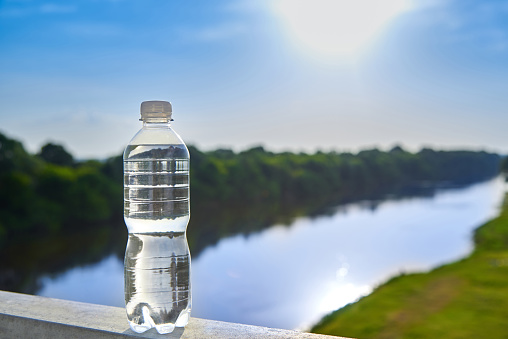 Pure transparent drinking water in a plastic bottle against the background of the river.